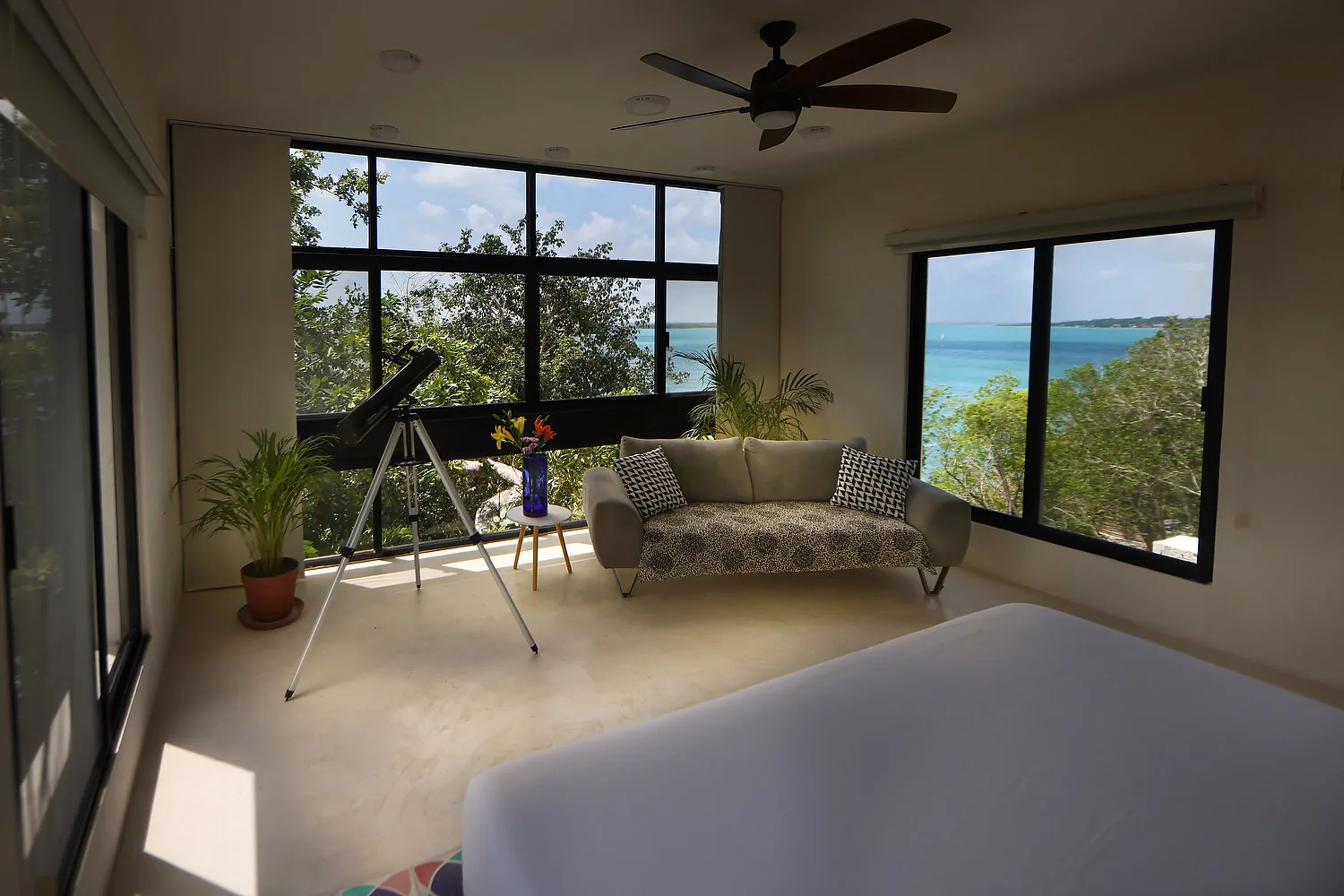 The Lagoon Suite, with a telescope, sofa and wide windows over the turquoise lagoon